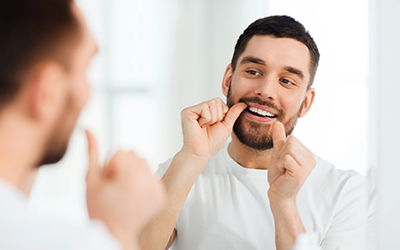 Man looking on the mirror while flossing his teeth