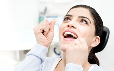 Woman in dental chair flossing her own teeth