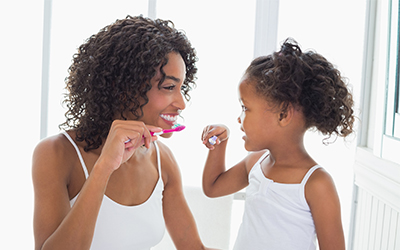 A mother brushing her teeth with her daughter before bed