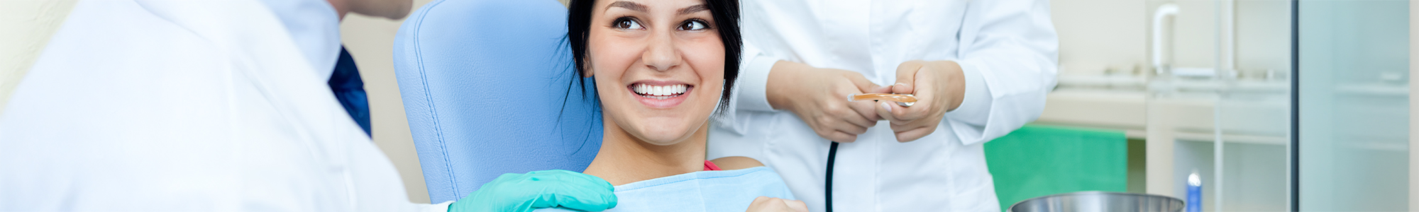 Close up of woman sitting in dental chair with dental professional on either side of her chair. 